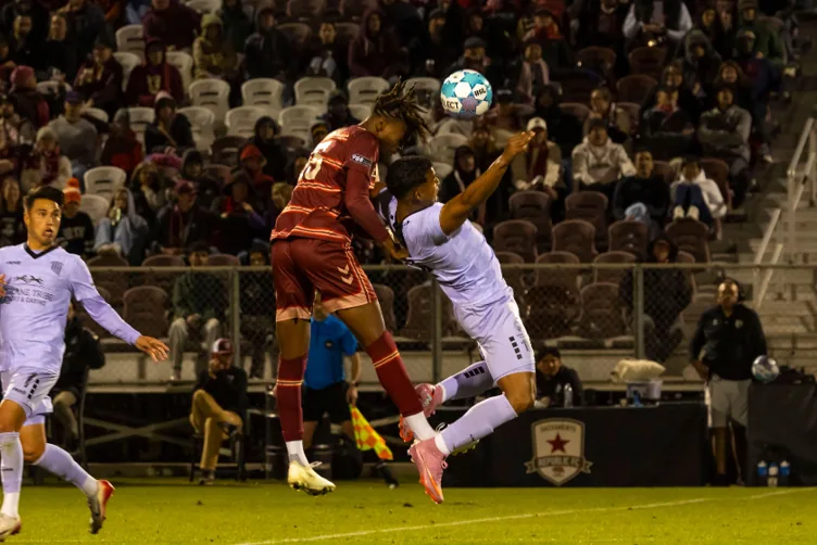 Football players contesting a header during a night match